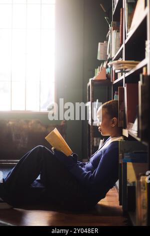 Fokussierte junge Frau, die Buch liest, während sie in der Nähe des Regals im Buchladen sitzt Stockfoto