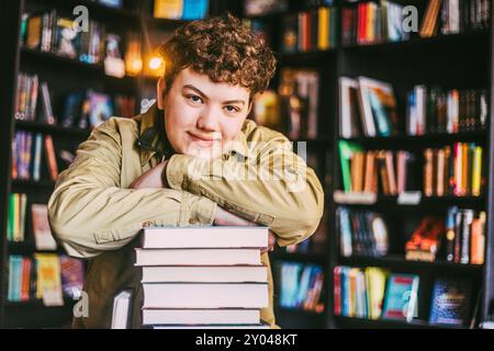 Porträt eines lächelnden jungen Mannes mit lockigen Haaren, der sich auf einen Stapel Bücher im Buchladen stützt Stockfoto