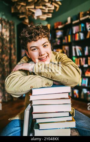 Lächelnder junger Mann, der sich auf einen Stapel Bücher stützt, während er im Buchladen sitzt Stockfoto