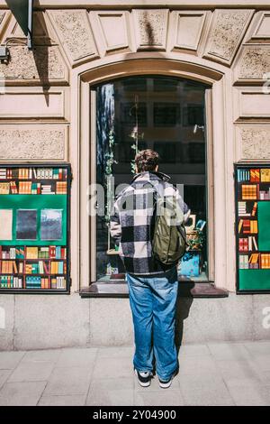 Rückansicht eines Mannes mit Rucksack, der neben dem Fenster des Buchladens steht Stockfoto