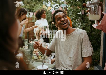 Ein glücklicher junger Mann isst Salat und redet mit Freunden auf einer Hinterhof-Party Stockfoto