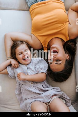 Direkt darüber erschossen glückliche Mutter und Tochter lachend, während sie zu Hause auf dem Sofa liegen Stockfoto