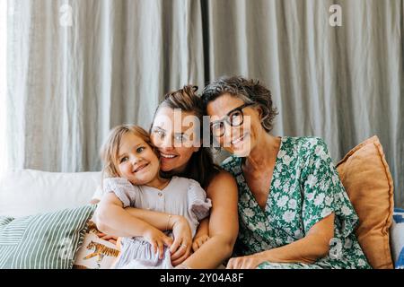 Porträt einer lächelnden Mutter, die mit Tochter und älterer Frau zu Hause auf dem Sofa sitzt Stockfoto