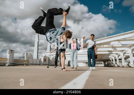 Sportlicher junger Mann beim Handstand, während männliche und weibliche Freunde auf dem Parkplatz unter bewölktem Himmel jubeln Stockfoto