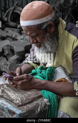 Ein älterer muslimischer Mann sitzt auf der Straße und schaut auf sein Handy. Ein alter Mann mit grauem Bart verbringt Zeit mit seinem Smartphone. Das Konzept der Technologienutzung Stockfoto