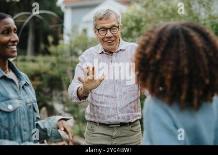 Lächelnder Seniorenmann mit Brille und grüßt Freunde auf einer Gartenparty Stockfoto