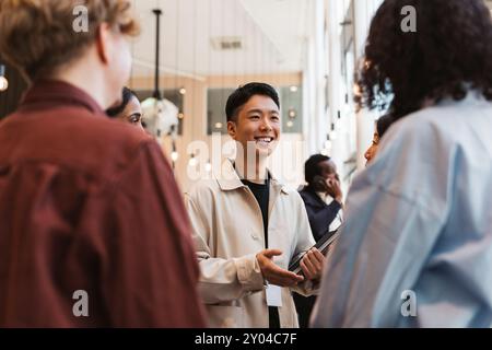 Lächelnder junger Unternehmer, der mit einer Gruppe von Delegierten während des Seminars im Kongresszentrum diskutiert Stockfoto