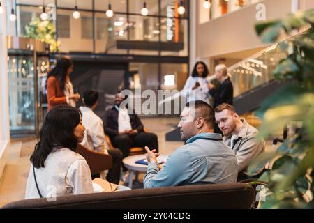 Multirassische Unternehmerinnen und Unternehmerinnen diskutieren Geschäftsstrategien, während sie in der Lobby des Kongresszentrums sitzen Stockfoto