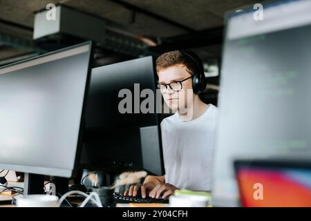 Junger männlicher Computerprogrammierer, der auf dem Desktop-PC sitzt und im Büro auf dem Schreibtisch sitzt Stockfoto
