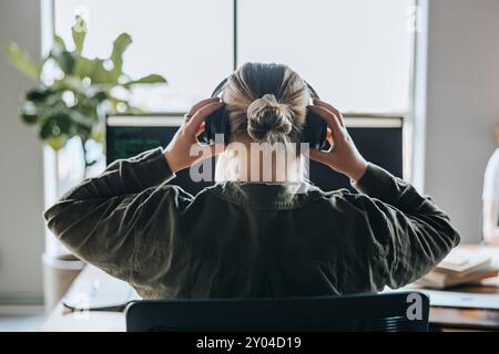 Rückansicht einer Programmiererin, die Kopfhörer trägt, während sie im Technikbüro sitzt Stockfoto