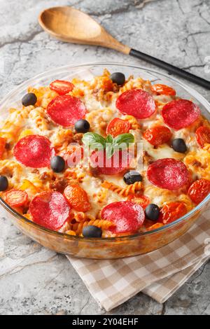 Pizza-Auflauf Pasta gebacken in einer Tomatensauce mit Käse, Würstchen, Paprika und Oliven in einer Glasschale auf dem Tisch. Vertikal Stockfoto