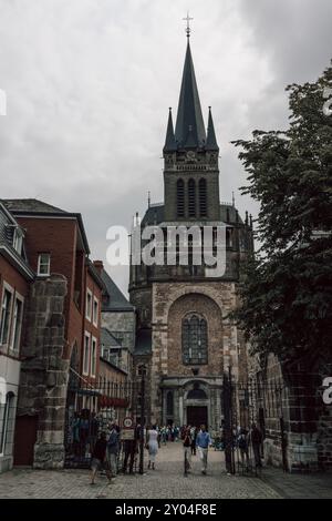 Menschen - Touristen und Gläubige - vor dem Eingang des Aachener Doms in Deutschland an einem bewölkten Sommersonntag nach einem hektischen Gottesdienst. Stockfoto