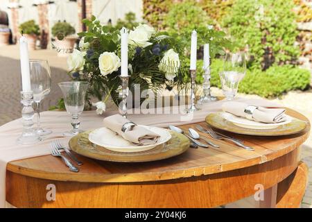 Kerzen und Vase mit weißen Rosen auf einem runden Tisch in der Nähe von Weingläsern während der Hochzeit im Garten Stockfoto