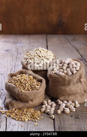 Getreide für eine gesunde Ernährung, Weizen, Haferflocken und Kichererbsen in Säcken auf rustikalem hölzernem Hintergrund Stockfoto