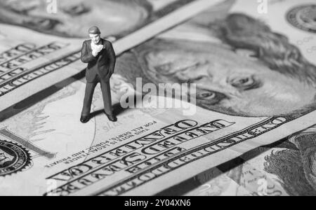 Miniaturfigur Geschäftsmann mit 100-Dollar-Banknote auf dem Hintergrund. Konzept Stockfoto