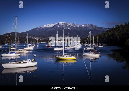 Boote und Reflexionen in Lindisfarne, Hobart, Tasmanien, Australien im Winter mit Blick auf den schneebedeckten Mount Wellington Stockfoto