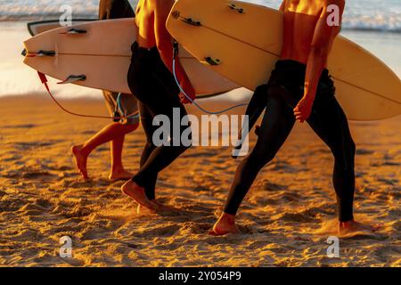 Zwei Männer laufen am Strand mit Surfbrettern. Die Surfbretter sind gelb und weiß. Der Strand ist sandig und der Himmel ist orange Stockfoto