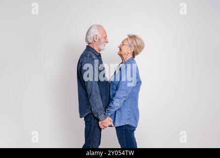 Seitenansicht eines romantischen älteren Paares, das Hände hält und sich vor weißem Hintergrund ansieht Stockfoto