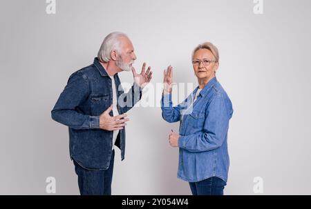 Eine ältere Frau zeigt eine Stop-Geste zu einem frustrierten Ehemann, während sie auf weißem Hintergrund streitet Stockfoto