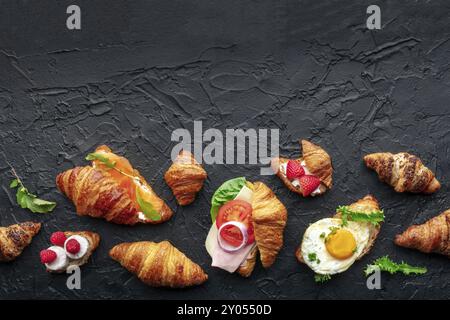 Croissant-Sandwichsortiment. Verschiedene gefüllte Croissants, über dem Kopf flacher Lay-Shot auf schwarzem Schieferhintergrund. Mit Schinken, Lachs, Ei usw. gefüllte Brötchen Stockfoto