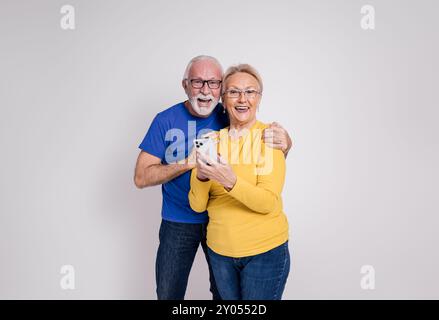 Porträt von aufgeregtem reifem Ehemann und Ehefrau mit Handy und Lachen auf weißem Hintergrund Stockfoto