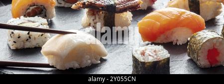 Sushi mit Stäbchen-Panorama. Weißer Fisch und Lachs-Nigiri auf schwarzem Hintergrund, japanische Küche auf einem Teller in einem asiatischen Restaurant Stockfoto