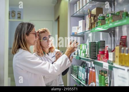 Zwei Apotheker in weißen Mänteln und Gläsern überprüfen und untersuchen Produkte in einem Apothekenregal Stockfoto