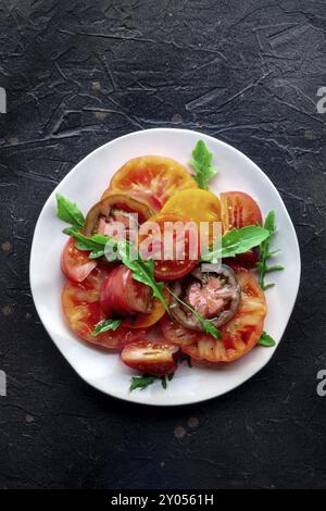 Frische Tomaten und Rucolasalat. Eine Vielzahl von Tomaten verschiedener Art, von oben mit Rucolablättern geschossen. Gesundes Sommeressen, Top-Shot Stockfoto