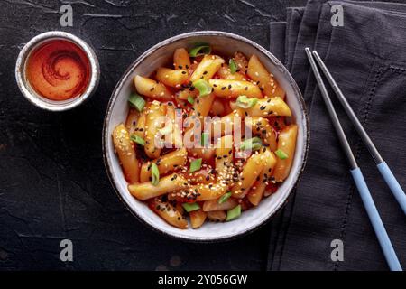 Tteokbokki oder Topokki, koreanisches Street Food, würzige Reiskuchen, flacher Schuss über Kopf mit Stäbchen und einem Getränk Stockfoto