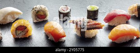 Sushi-Panorama. Nigiri mit Aal, Lachs und Thunfisch, Rolle mit Avocado und Maki mit Gurke auf schwarzem Hintergrund, japanisches Essen auf einem Teller in einem asiatischen Stockfoto