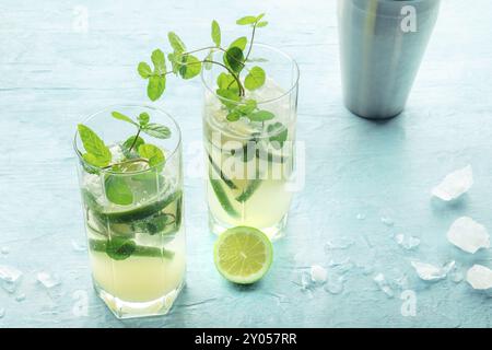 Mojito-Cocktail, zwei Gläser. Sommerliches kaltes Getränk mit Limette, frischer Minze und Eis. Kühles Getränk auf blauem Hintergrund mit einem Schüttler Stockfoto