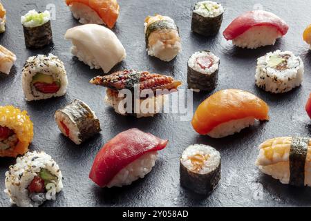 Sushi-Auswahl. Brötchen, Maki, Nigiri auf schwarzem Hintergrund, japanisches Essen. Lachs, Thunfisch, Aal, Garnelen mit Reis auf einem Teller in einem asiatischen Restaurant Stockfoto