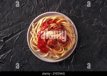 Fleischbällchen. Rindfleischbällchen, Overhead Shot mit Spaghetti-Pasta, Petersilie und Tomatensauce auf schwarzem Schieferhintergrund Stockfoto