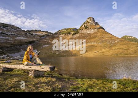 Der Augstsee und der Atterkogel auf dem Verlierer. Ein Wanderer sitzt auf einer Bank und liest ein Buch. Herbst, gutes Wetter, blauer Himmel. Altaussee, Bad Ausse Stockfoto