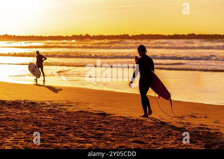 Ein Mann läuft am Strand mit einem Surfbrett. Die Sonne untergeht und schafft eine schöne und ruhige Atmosphäre Stockfoto