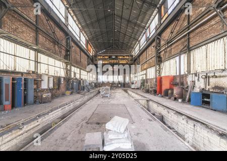 Große verlassene Werkstatt mit Schienen im Zentrum, umgeben von Ziegelmauern und Maschinen, Stahlwerk HF4, Lost Place, Dampremy, Charleroi, Provinz Stockfoto