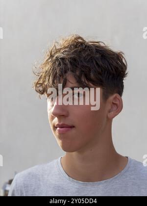 Porträt eines jungen Sportmannes mit lockigen braunen Haaren vor einer grauen Wand, der in die Kamera blickt Stockfoto