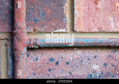 Detail der alten Kupferwasserrohre, die Korrosion und Kalk ausgesetzt sind, an der Außenseite eines Gebäudes vor einer verwitterten Risswand und einer abblätternden Ziegelwand. Stockfoto