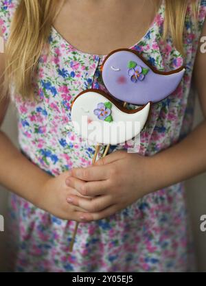 Ein kleines Mädchen, das violette und weiße Kekse hält, die Vögel in der Hand Stockfoto