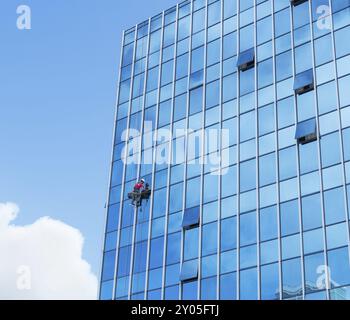 Fensterreiniger, der an einer aufgehängten Glasfassade arbeitet. Schwerarbeitskonzept Stockfoto