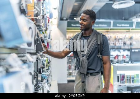 Seitenansicht dreiviertel Foto eines fröhlichen afrikanischen Mannes, der Kopfhörer im Elektronikgeschäft überprüft Stockfoto