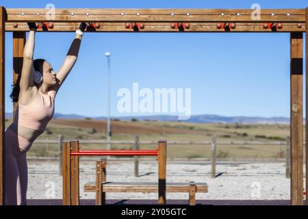 Porträt einer athletischen Frau, die an einem sonnigen Tag mit Kopfhörern und Sportbekleidung an parallelen Gittern hochzieht Stockfoto