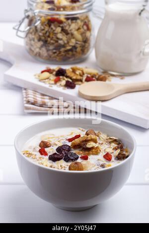 Schüssel mit hausgemachtem Müsli mit Nüssen, Beeren, getrockneten Früchten, Milch und Honig auf weißem Hintergrund aus Holz. Gesundes Frühstück Stockfoto