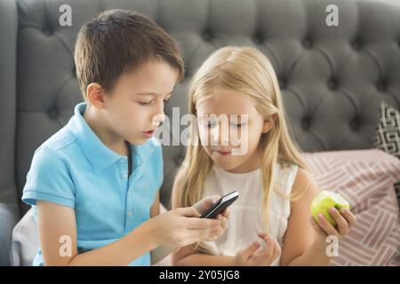 Kleiner Bruder und Schwester auf dem Sofa Handy spielen zusammen. Family Portrait Stockfoto