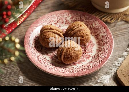 Drei selbstgemachte Weihnachtskekse in Form von Nüssen gefüllt mit Kakaocreme auf einem roten Teller Stockfoto