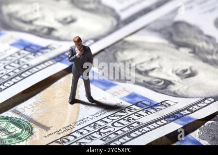 Miniaturfigur Geschäftsmann mit 100-Dollar-Banknote auf dem Hintergrund. Konzept Stockfoto