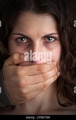 Nahaufnahme einer Hand, die einen Frauenmund bedeckt. Konzept häuslicher Gewalt oder Entführung. Dunkle Stimmung Stockfoto