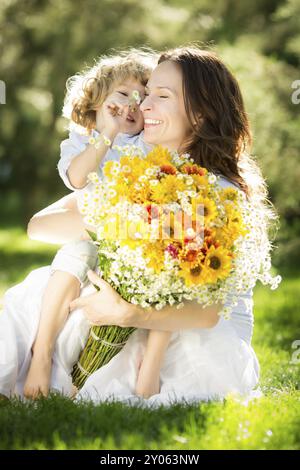 Glückliches Kind und Frau mit Blumenstrauß auf grünem Gras. Muttertagskonzept Stockfoto