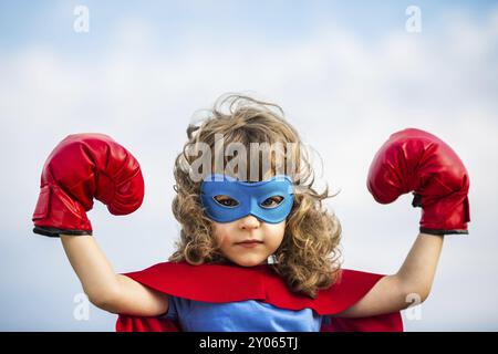 Superheldenkind mit Boxhandschuhen vor blauem Himmel. Mädchenmacht und Feminismuskonzept Stockfoto