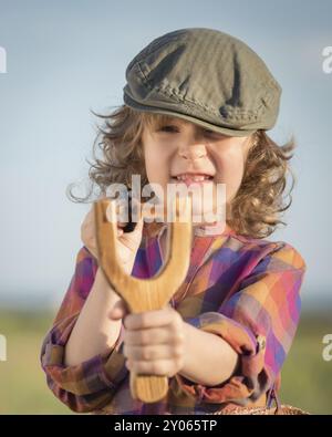 Lustiges Kind, das Holzschleuder vor blauem Sommerhimmel schießt Stockfoto